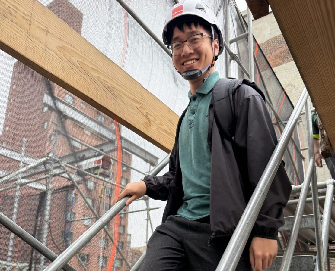 A design professional in a hard had descends a scaffolding staircase
