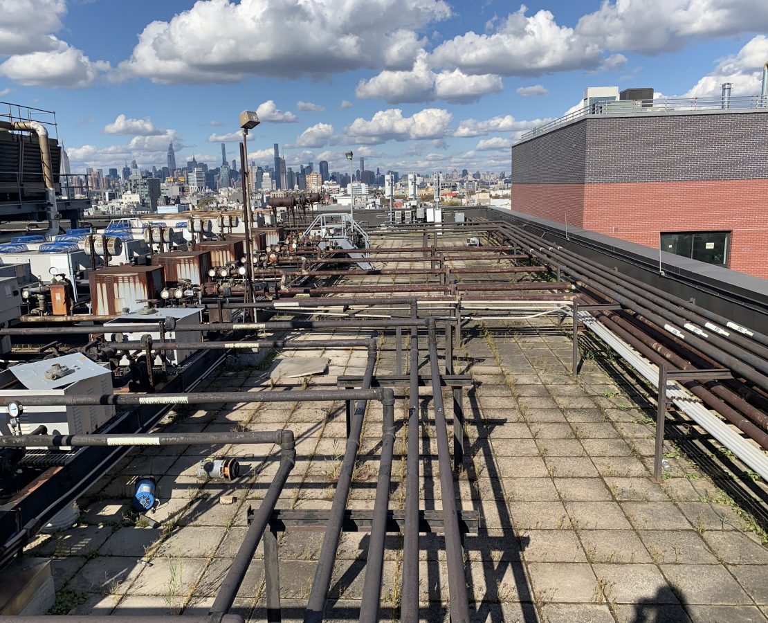 Roof with pipes and rooftop equipment with blue cloudy sky in background