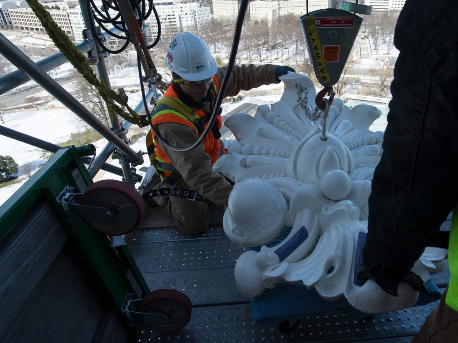 A construction worker guides a restored cast iron element back into place at the US Capitol Dome.