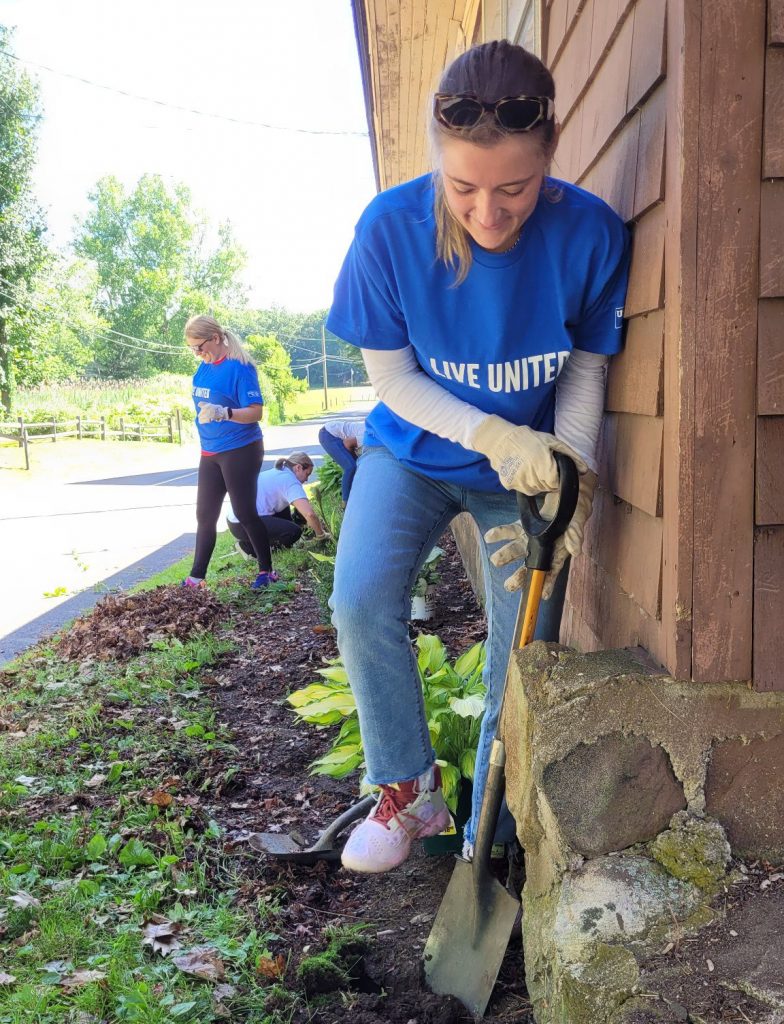 Chelsea Doyle in a blue shirt leaning against a wall with a shovel