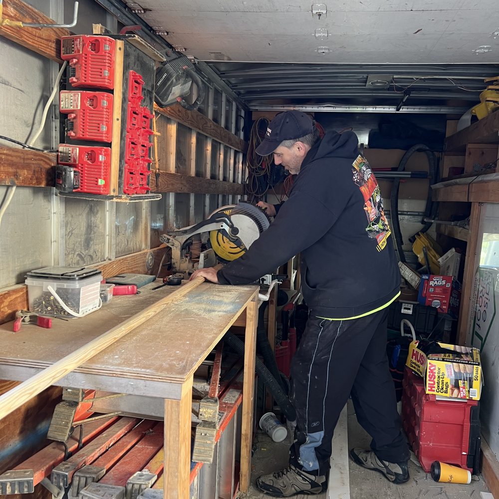 A man cuts wood with a circular saw inside a trailer
