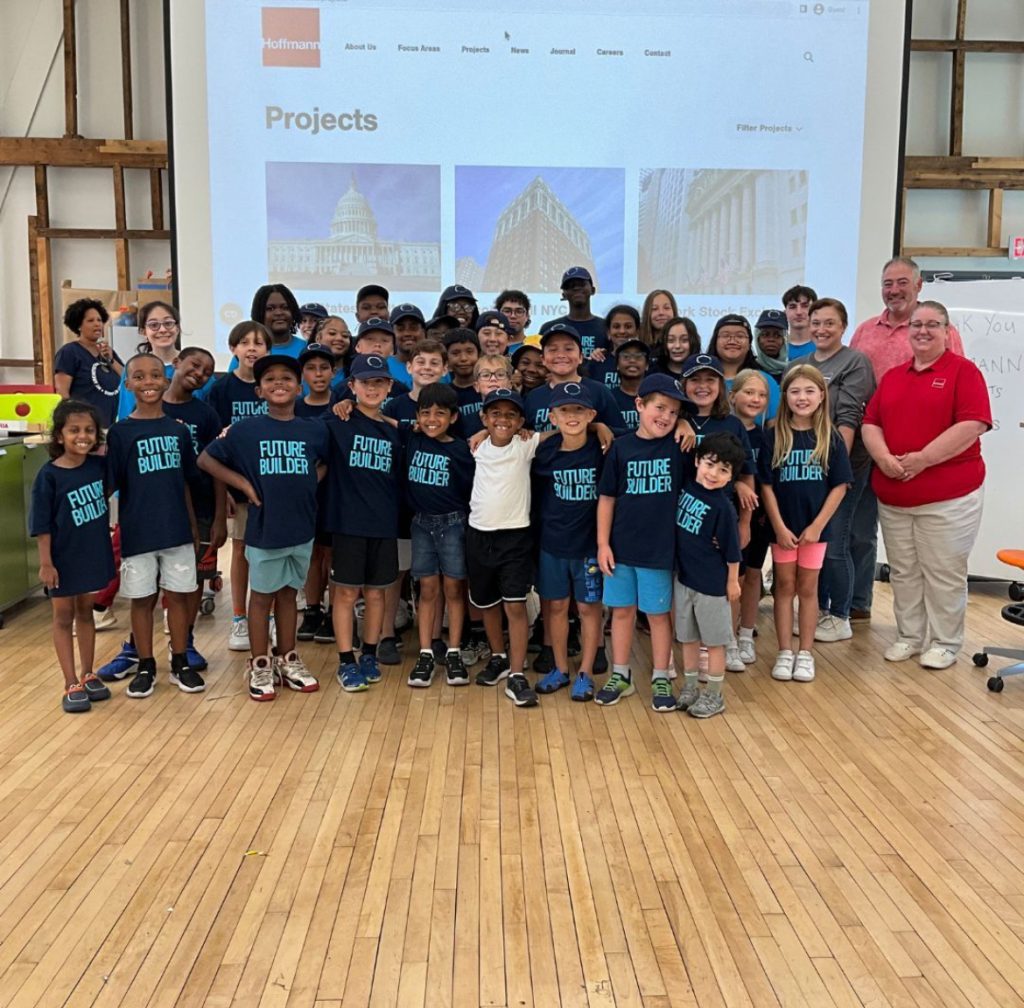 Campers pose for the camera with architect mentors in front of a screen