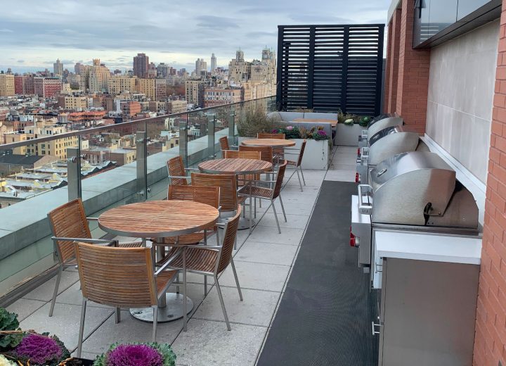 A rooftop with tables, chairs, and grills that overlooks New York City