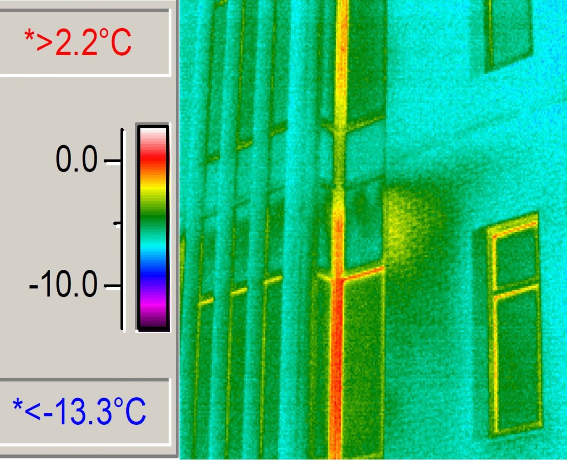 Part of a pair of images, this one shows an infrared camera view of an exterior masonry and glass curtain wall with bright colors indicating temperature