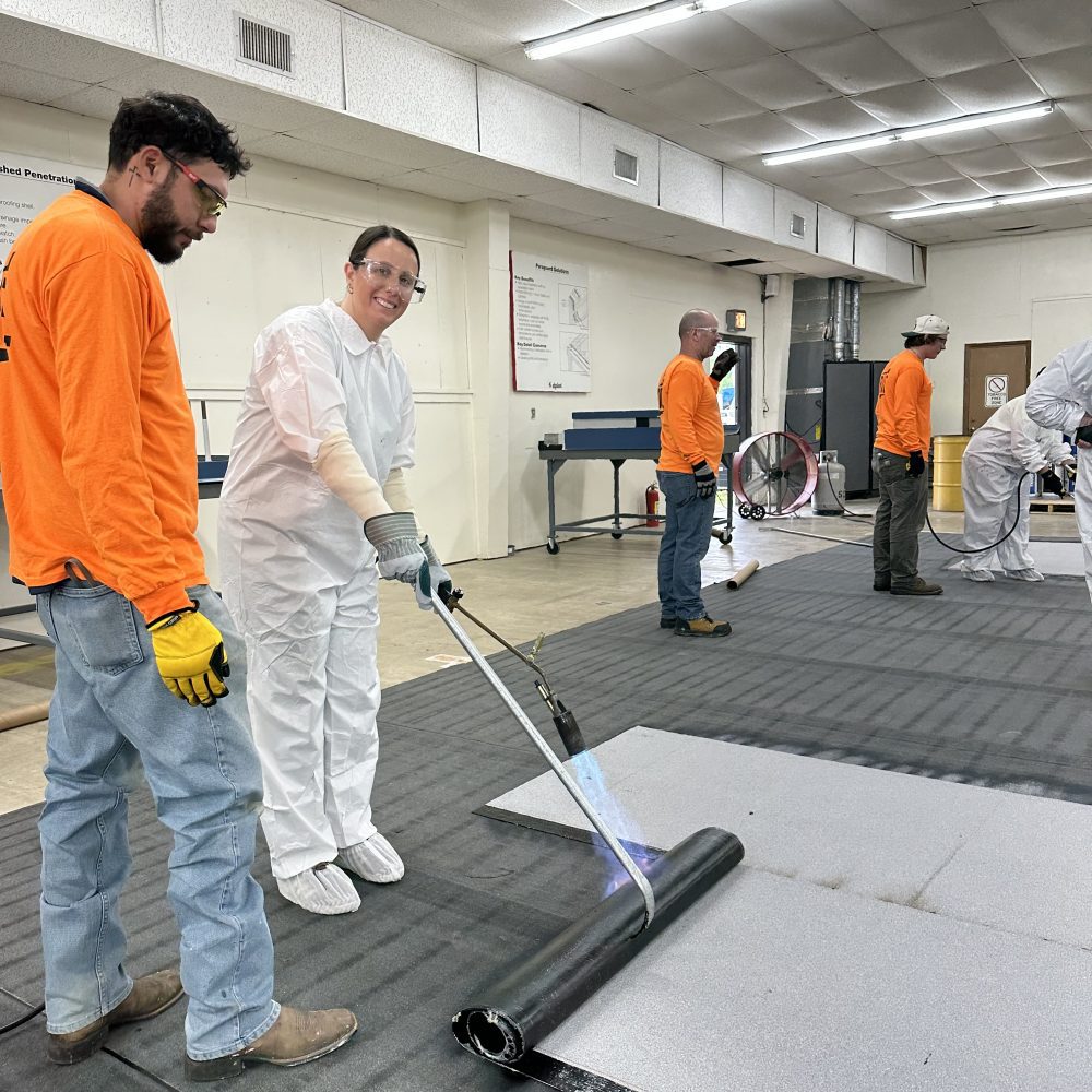 An architect in protective clothing practices torch-applying a roof membrane at a roofing plant
