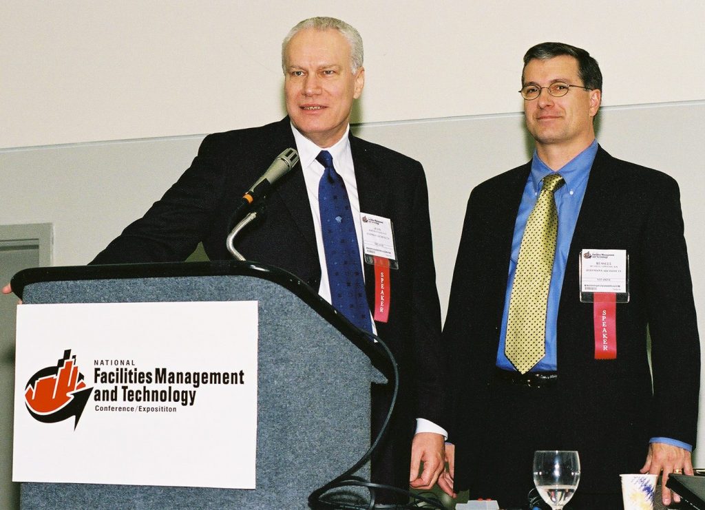Architects John Hoffmann and Russell Sanders standing at a podium delivering a lecture.